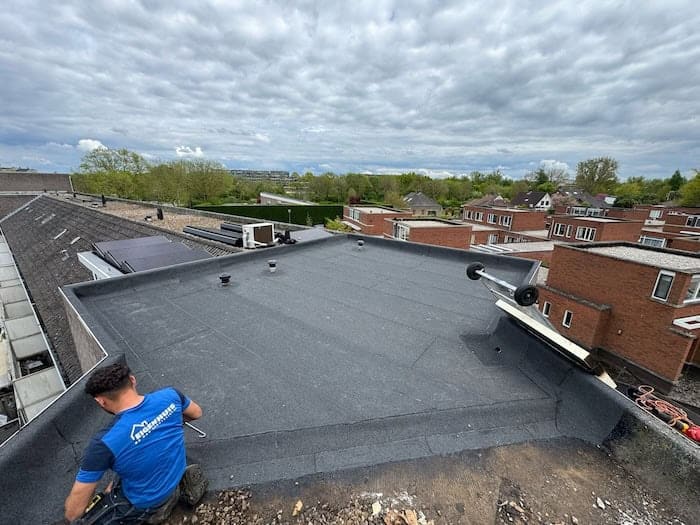 Dakdekker renoveert platte dak met bitumen in woonwijk onder bewolkte hemel