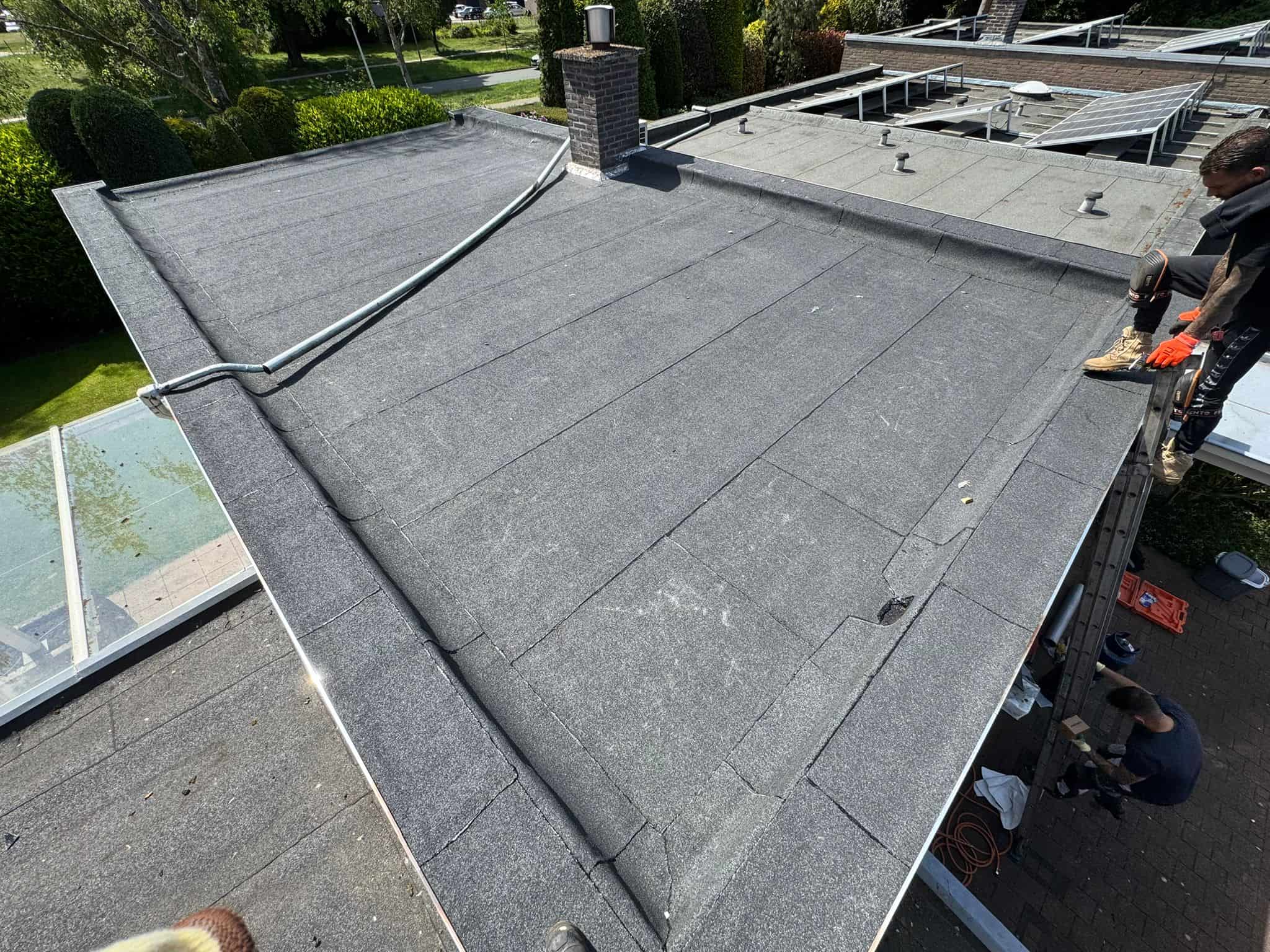 Dakdekkers brengen bitumen dakbedekking aan op plat dak tijdens onderhoudswerkzaamheden