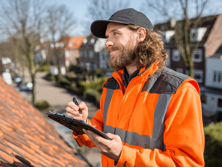 Dakinspecteur in oranje veiligheidsjas met clipboard controleert dak in woonwijk