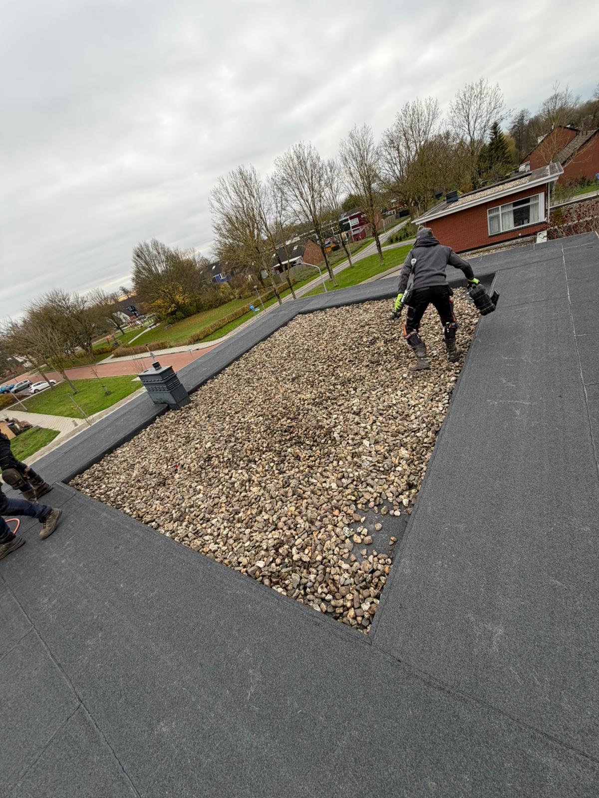 Dakdekkers leggen bitumen en grind op nieuw plat dak in woonwijk