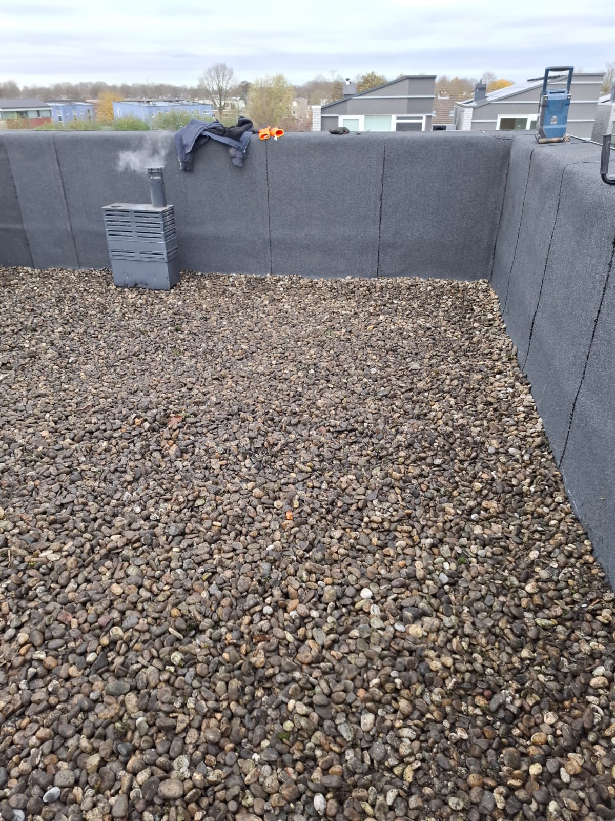 Plat dak met grind als ballast, geïnstalleerde ventilatieschoorsteen en gereedschap op rand