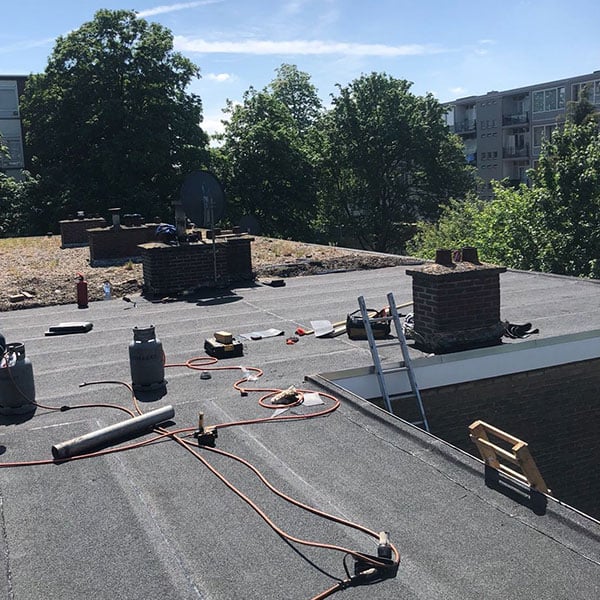Plat dak renovatie met gasbranders, ladder, schoorstenen en groene omgeving