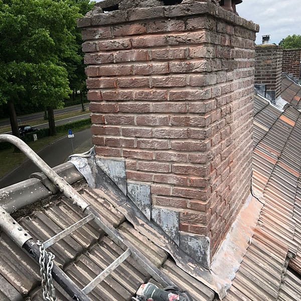 Bakstenen schoorsteen met verse loodslabben tijdens dakrenovatie met grijze keramische dakpannen