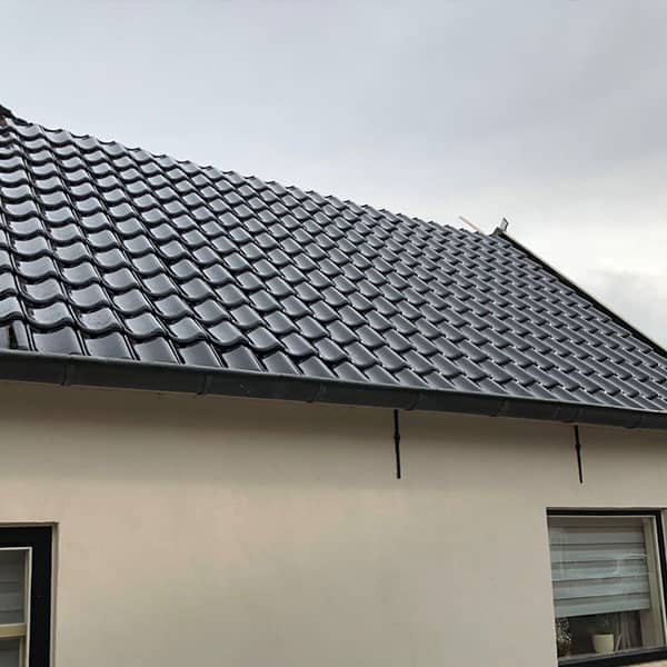 Moderne woning met nieuwe glanzende zwarte dakpannen op witte gevel bij bewolkte hemel