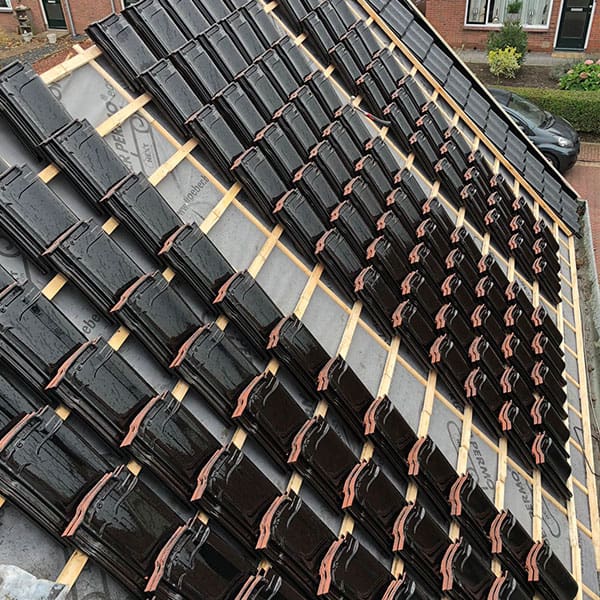 Rijen zwarte keramische dakpannen op houten daklatten klaar voor montage