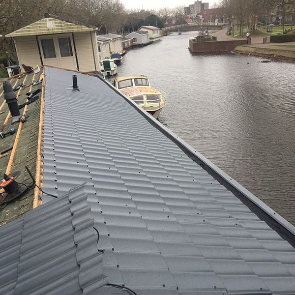 Nieuw metalen dak op woonboot langs rustig stadskanaal met aanlegsteiger