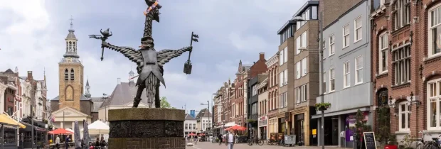 Standbeeld met vleugels en weegschaal op gezellig stadsplein met kerk en winkels