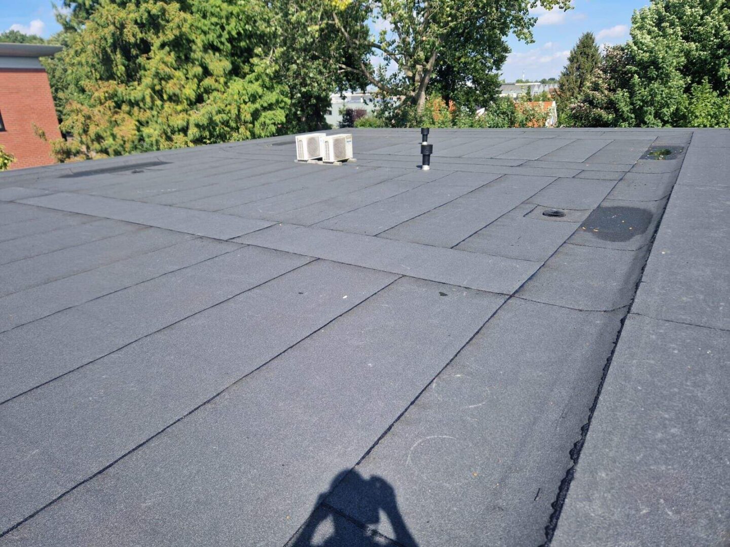 Platte bitumen dak met ventilatiepijp en airco-units bij groene omgeving