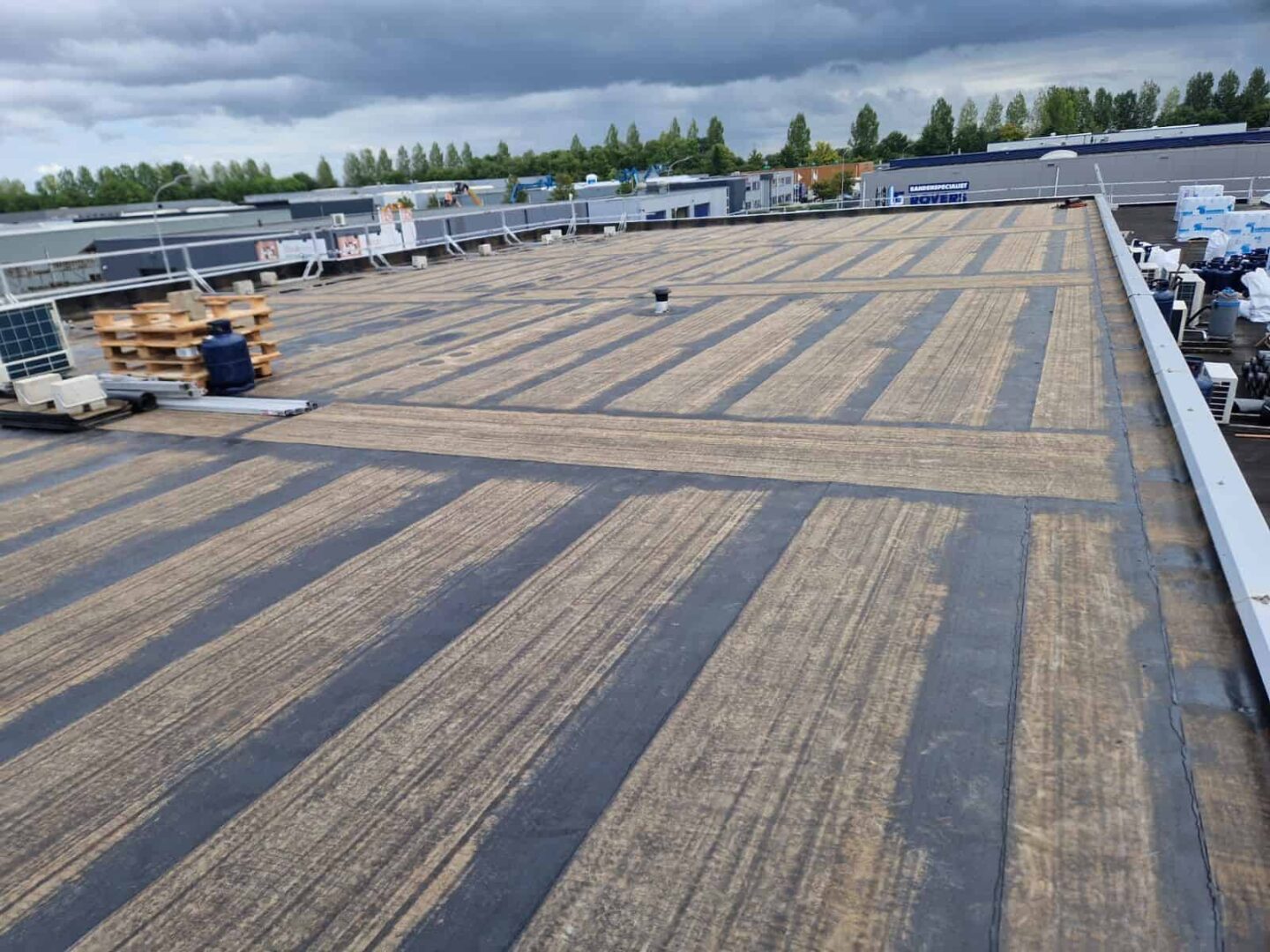 Groot industrieel plat dak in renovatie met blootliggende dakbanen, bouwmaterialen en bewolkte hemel