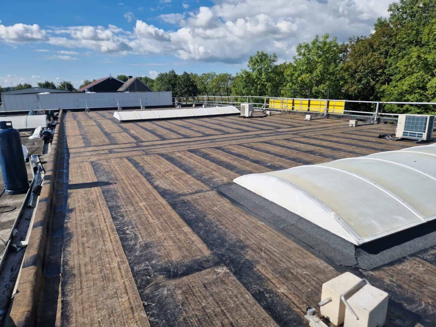 Plat dak met nieuwe bitumen dakbedekking, lichtkoepels en airco-units onder blauwe lucht