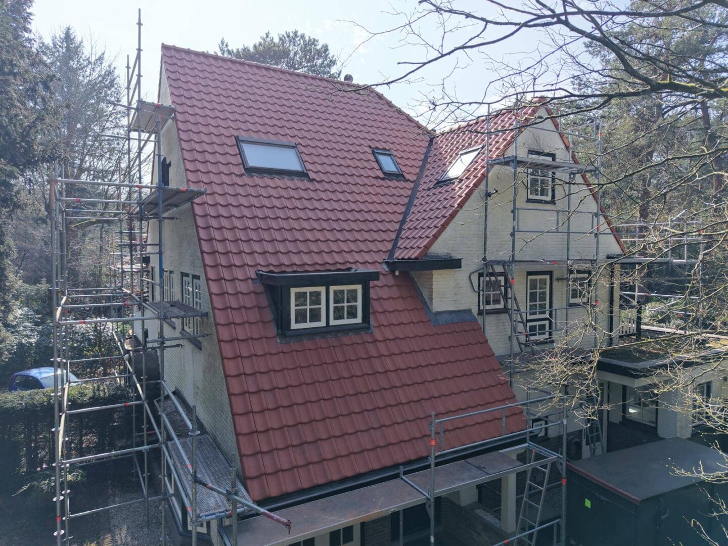 Witte villa met rood pannendak en steigers voor buitenrenovatie in bosrijke omgeving
